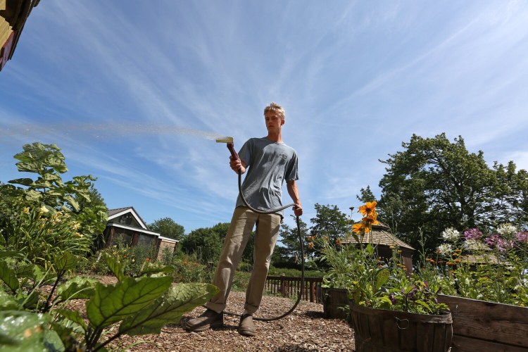 Aidan Connor, an employee at Jordan Farm in Cape Elizabeth, waters plants outside the farm's market on Sunday. "It's been really hot and the sun has just been blaring down," he said.
