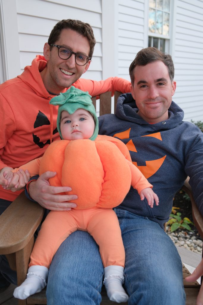 Jordan Wood is pictured with his husband, Jake, and their 1-year-old daughter, Ella, in a family pumpkin costume photo from October 2025.